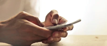 Hände, die ein Smartphone auf einem Holztisch bedienen