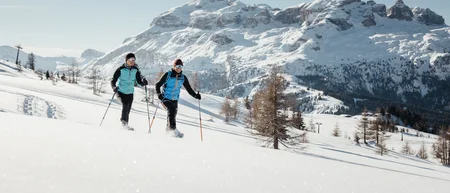 Zwei Personen beim Schneeschuhwandern vor schneebedeckten Bergen