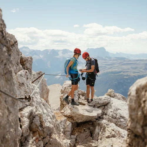 Auf zum Wandern in Alta Badia, rings ums Nature Hotel Delta! Zwei Kletterer mit Helmen und Rucksäcken auf felsigem Berggipfel