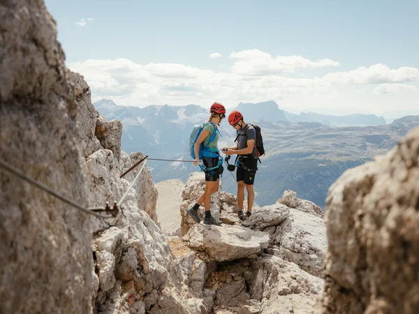 Auf zum Wandern in Alta Badia, rings ums Nature Hotel Delta! Zwei Kletterer mit Helmen und Rucksäcken auf felsigem Berggipfel