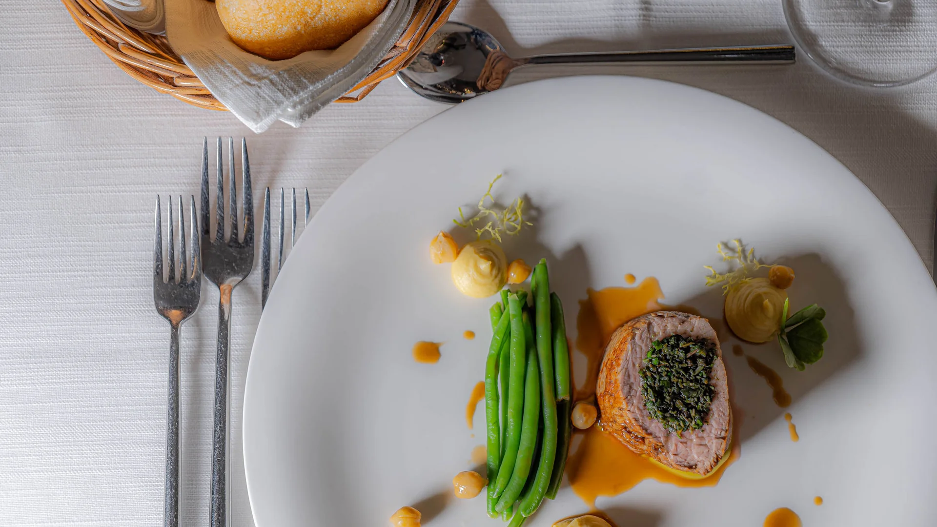 Gourmetgericht mit grünem Gemüse, Fleisch und Soße auf weißem Teller
