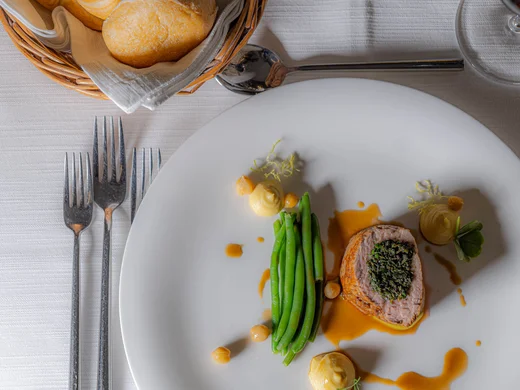 Gourmetgericht mit grünem Gemüse, Fleisch und Soße auf weißem Teller