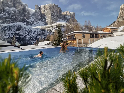 Menschen schwimmen im Außenpool mit Blick auf schneebedeckte Berge und Gebäude