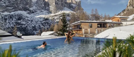 Menschen schwimmen im Außenpool mit Blick auf schneebedeckte Berge und Gebäude