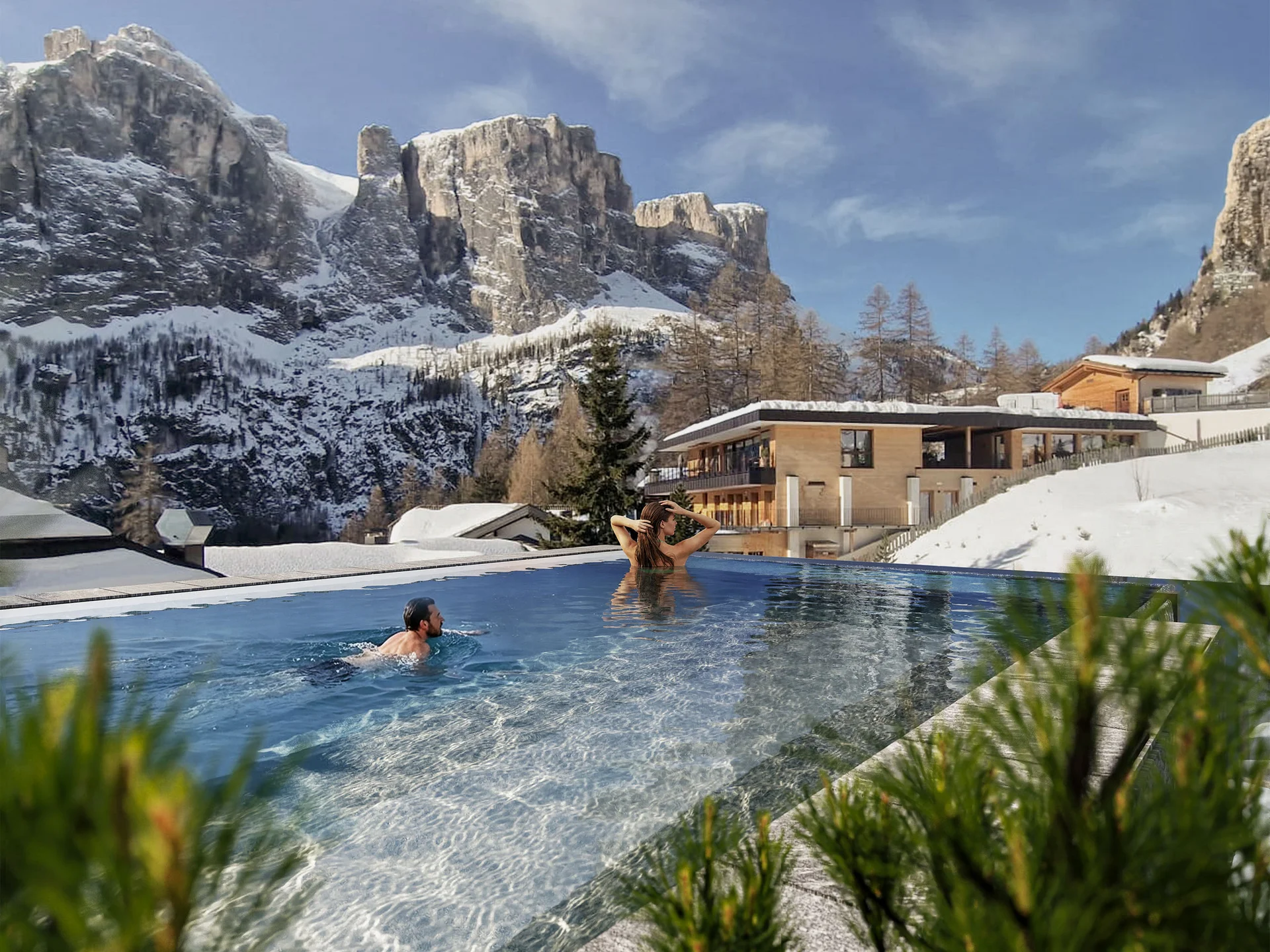 Unser Wellnesshotel in Alta Badia: das Nature Hotel Delta Menschen schwimmen im Außenpool mit Blick auf schneebedeckte Berge und Gebäude