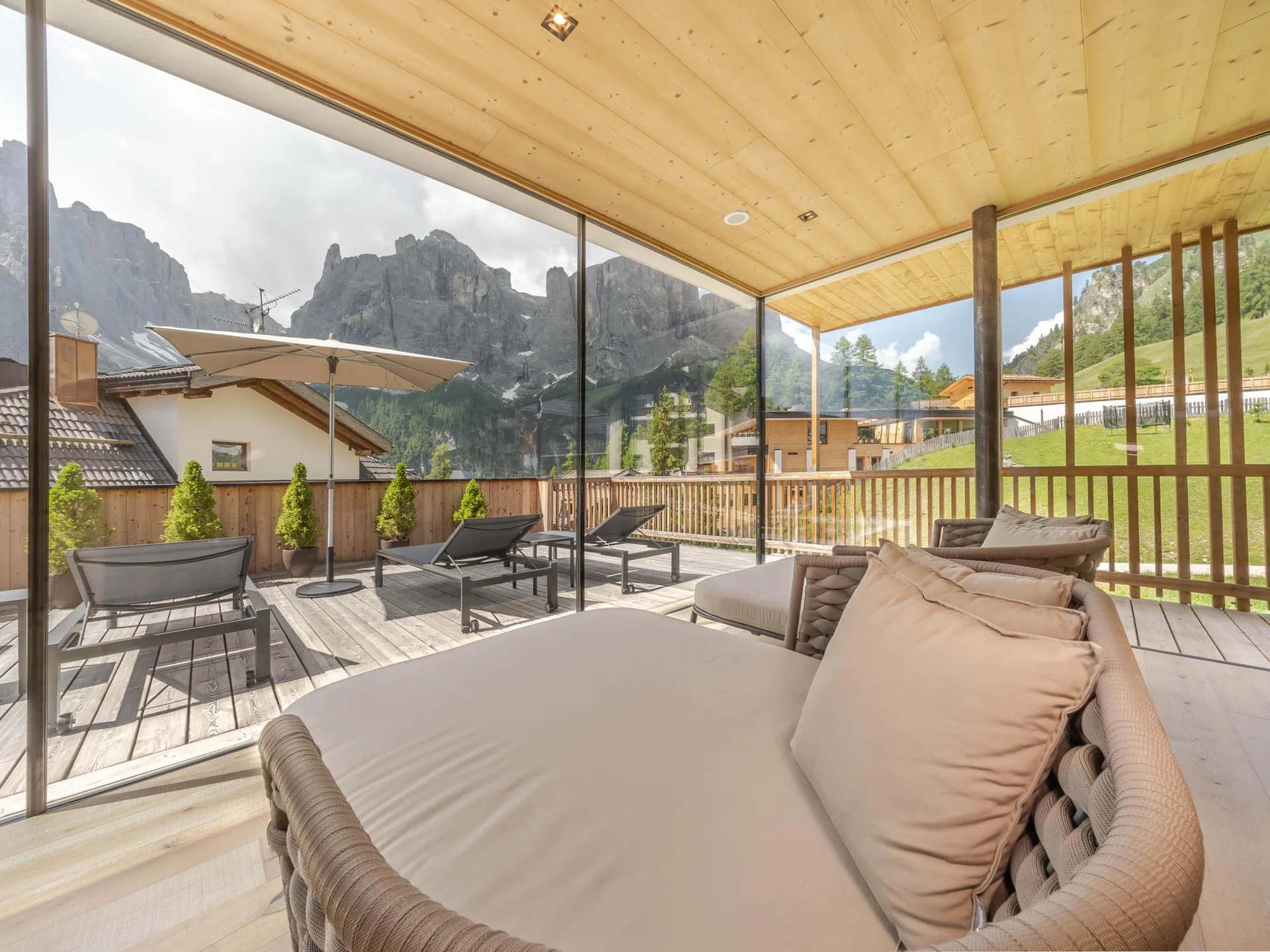 Unser Wellnesshotel in Alta Badia: das Nature Hotel Delta Terrasse mit Liegestühlen und Bergblick hinter Glaswand