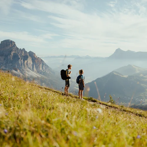 Zwei Wanderer mit Rucksäcken auf Bergwiese mit Blick auf Berge und Tal