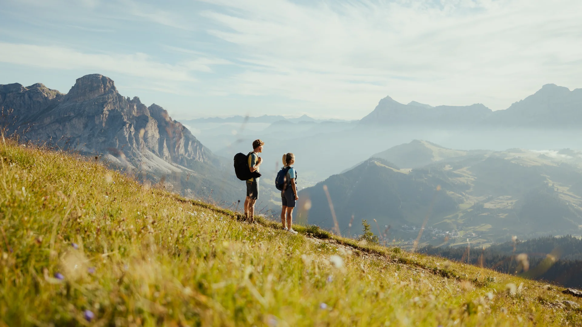 Die schönsten Eindrücke aus dem Nature Hotel Delta Zwei Wanderer mit Rucksäcken auf Bergwiese mit Blick auf Berge und Tal