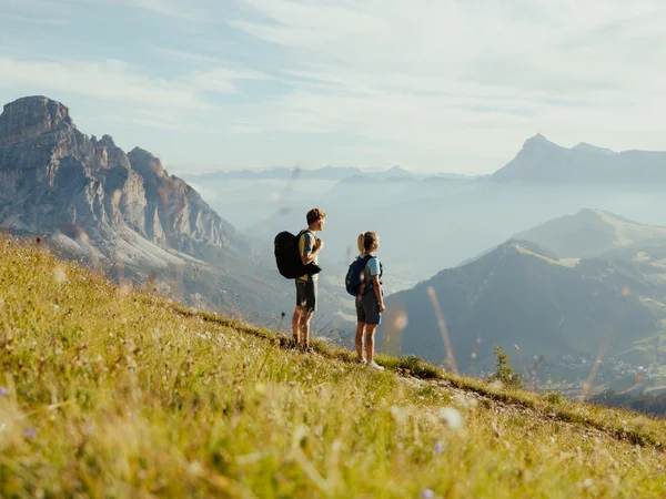 Zwei Wanderer mit Rucksäcken auf Bergwiese mit Blick auf Berge und Tal