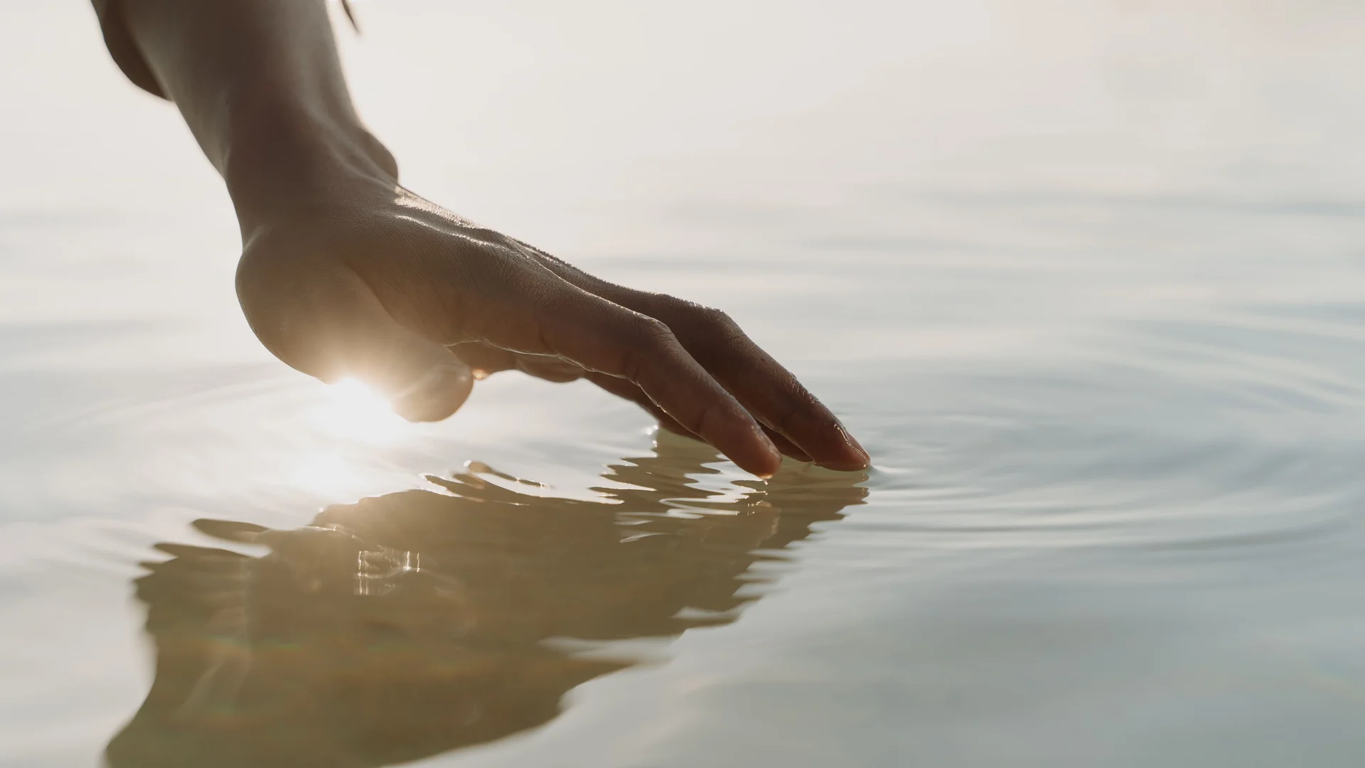 Unser Wellnesshotel in Alta Badia: das Nature Hotel Delta Hand berührt sanft die Wasseroberfläche bei Sonnenlicht