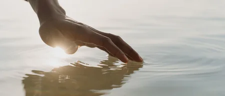 Hand berührt sanft die Wasseroberfläche bei Sonnenlicht