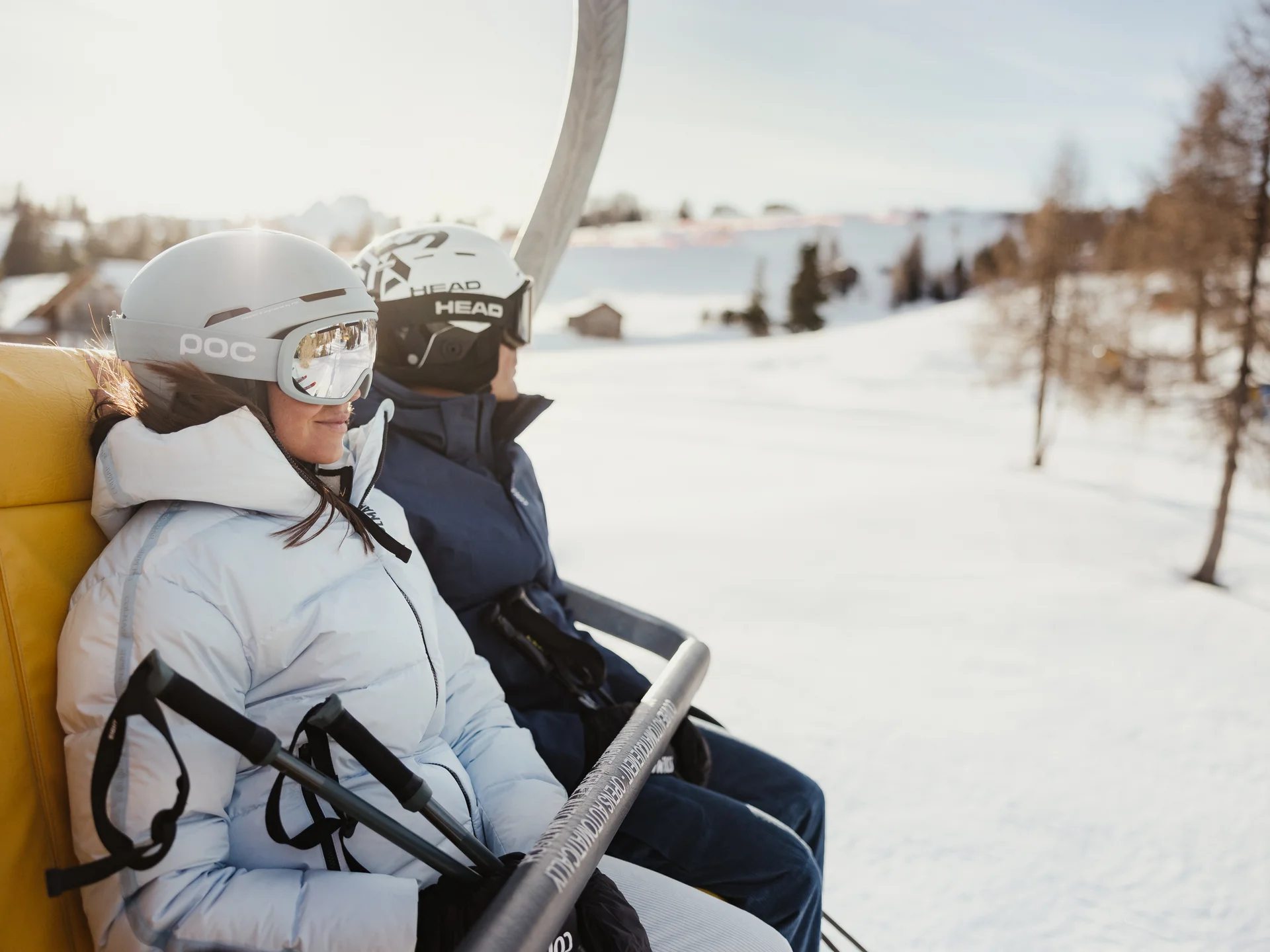 Zwei Skifahrer mit Helmen auf einem Skilift über verschneiter Landschaft