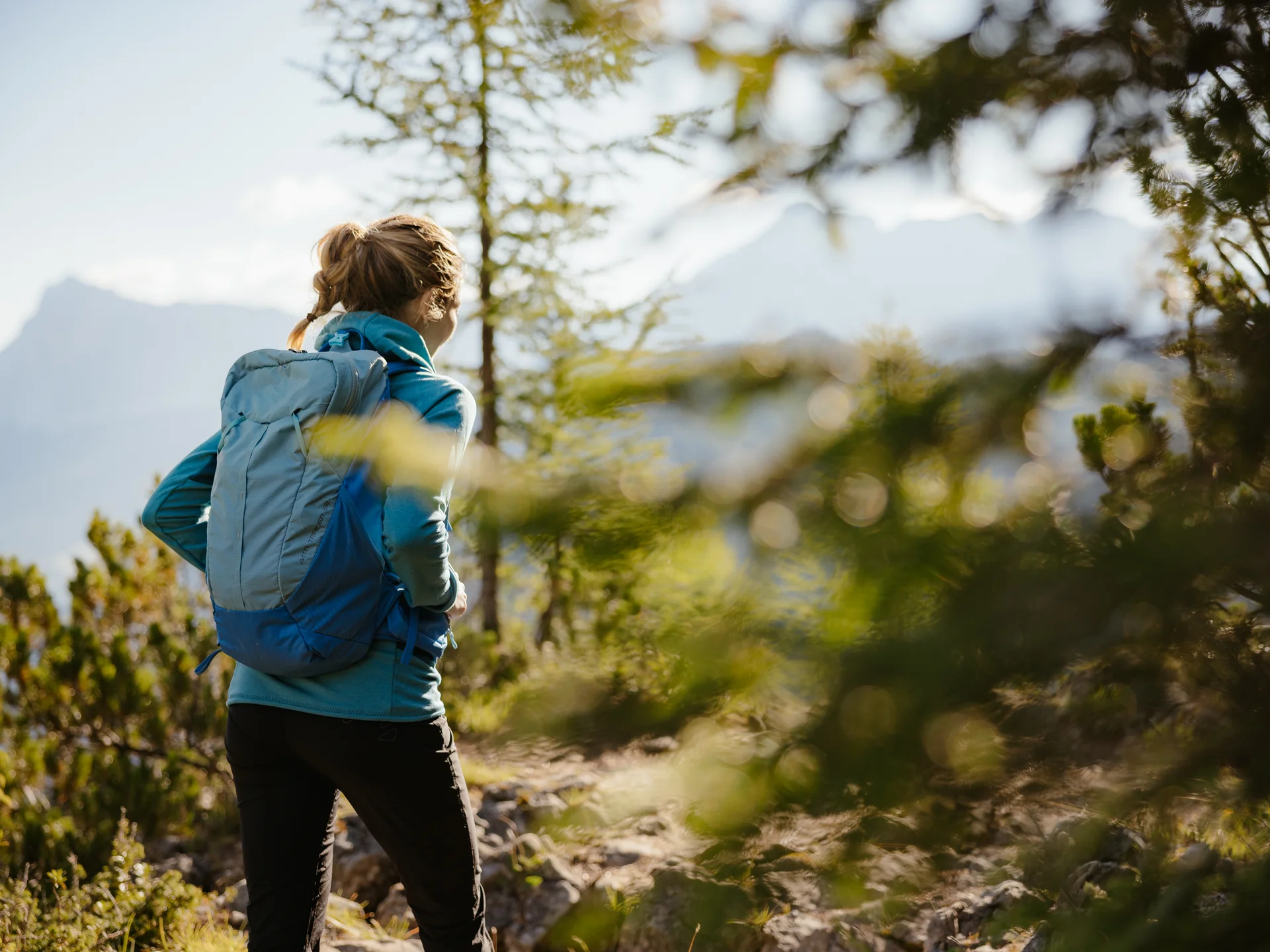 Frau mit Rucksack wandert auf einem Waldweg in den Bergen