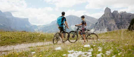 Zwei Radfahrer mit Mountainbikes auf einem Weg in blumiger Berglandschaft