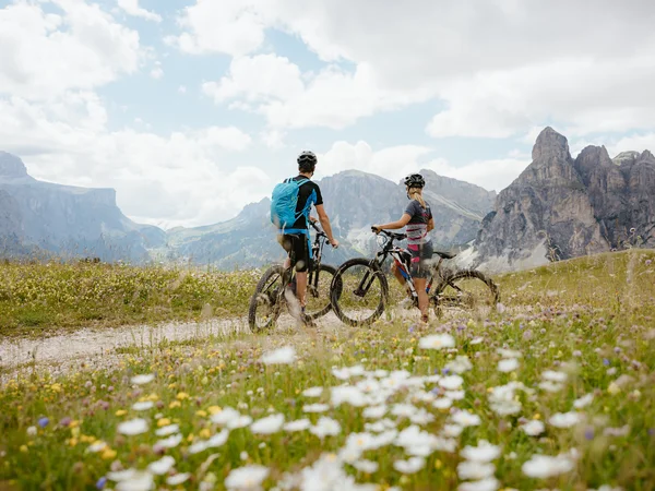 Auf zum Wandern in Alta Badia, rings ums Nature Hotel Delta! Zwei Radfahrer mit Mountainbikes auf einem Weg in blumiger Berglandschaft