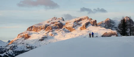 Zwei Skifahrer auf schneebedecktem Hügel mit Sonnenuntergang über Bergen