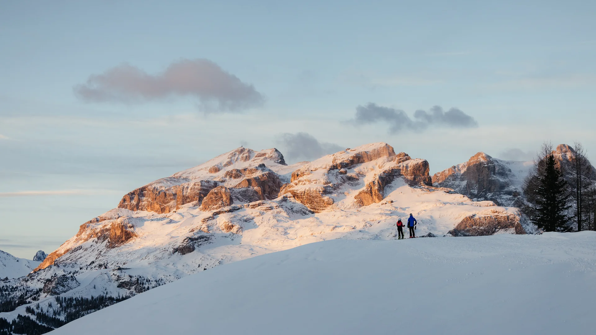 Das ist sehenswert in der Umgebung des Nature Hotel Delta. Zwei Skifahrer auf schneebedecktem Hügel mit Sonnenuntergang über Bergen