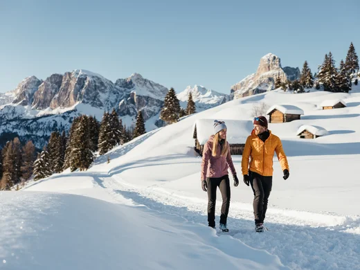 Den Winter in Alta Badia genießen – im Nature Hotel Delta Paar wandert auf verschneitem Weg in den Bergen bei Sonnenschein