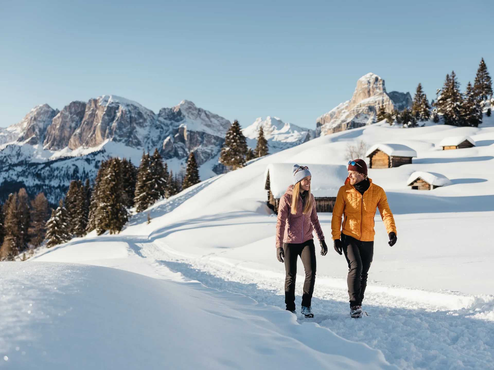 Paar wandert auf verschneitem Weg in den Bergen bei Sonnenschein