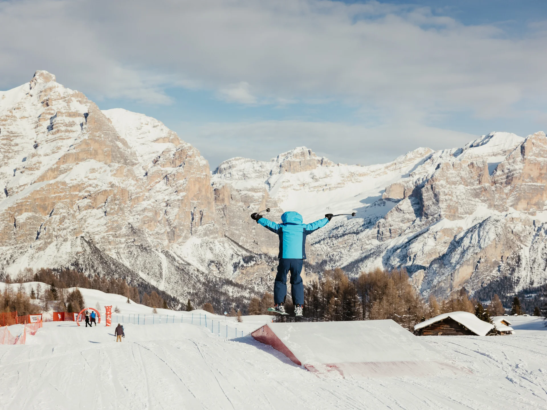 Kind in blauer Skibekleidung springt mit Skiern vor schneebedeckten Bergen