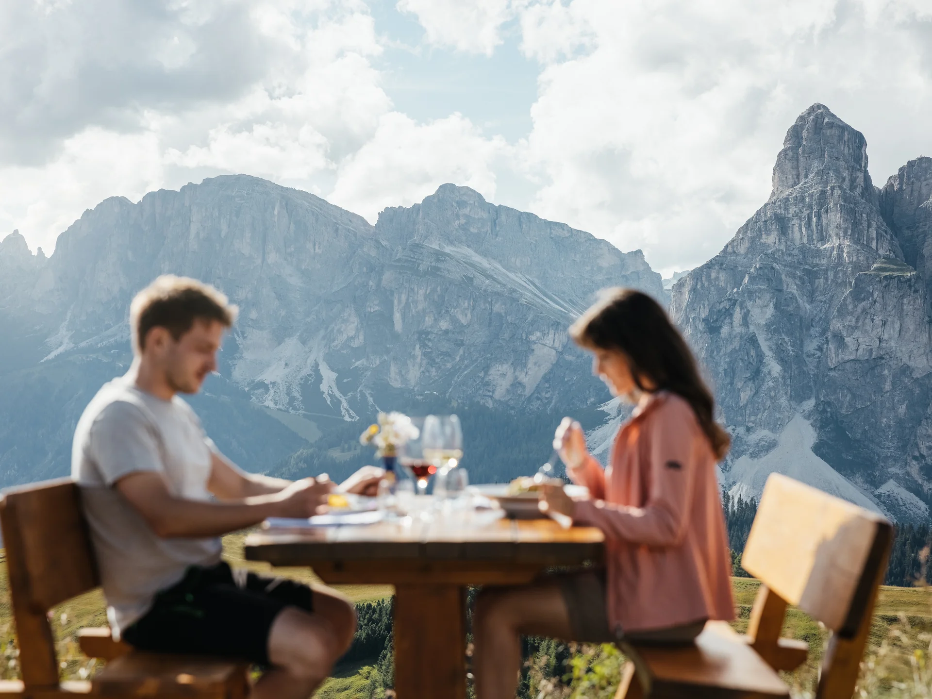 Paar isst draußen an Holztisch mit Bergpanorama im Hintergrund