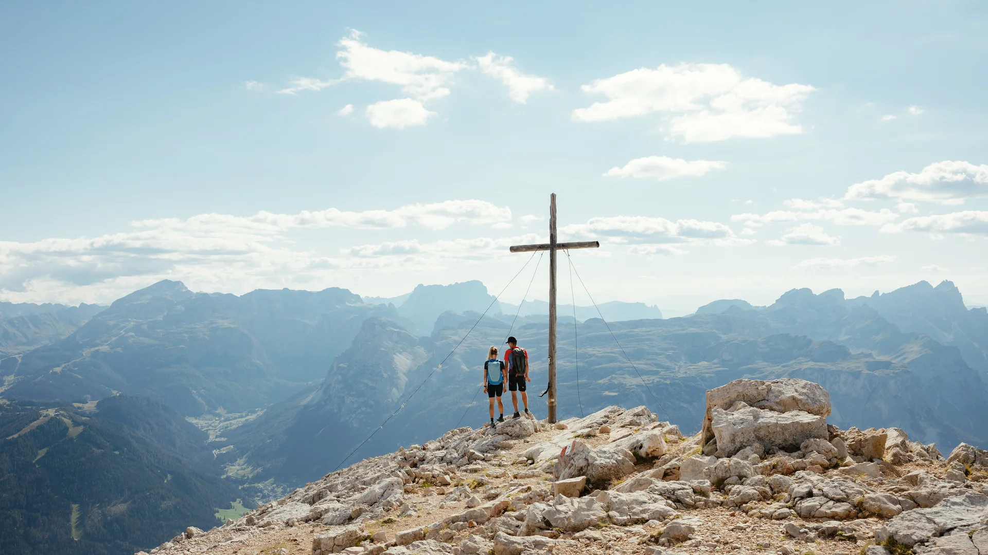 Das ist sehenswert in der Umgebung des Nature Hotel Delta. Zwei Wanderer stehen neben Gipfelkreuz mit Bergpanorama im Hintergrund