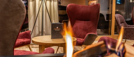 Gemütliche Sitzecke mit roten Sesseln und brennendem Kamin im Hotel