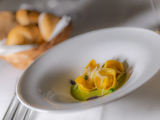 Teller mit Tortellini auf grüner Sauce und Brotkorb im Hintergrund