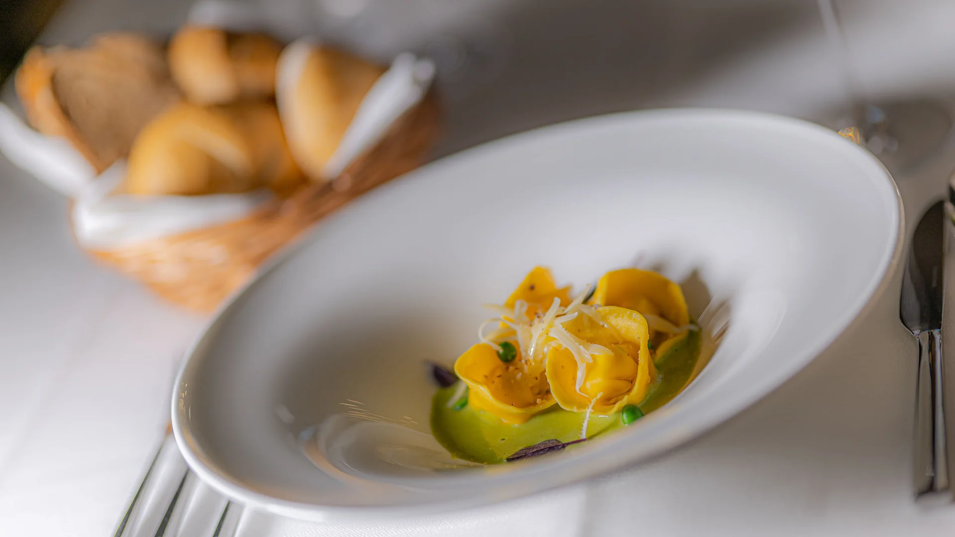 Die schönsten Eindrücke aus dem Nature Hotel Delta Teller mit Tortellini auf grüner Sauce und Brotkorb im Hintergrund