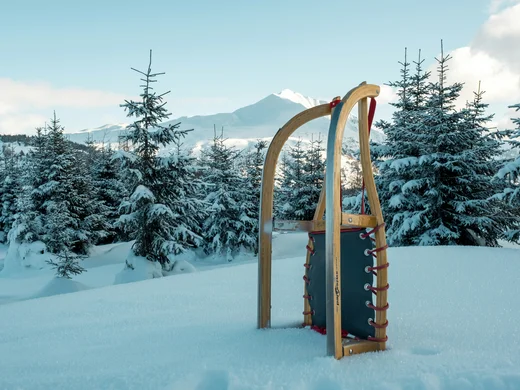 Den Winter in Alta Badia genießen – im Nature Hotel Delta Rodelschlitten steht im Schnee vor verschneiten Tannen und Bergen