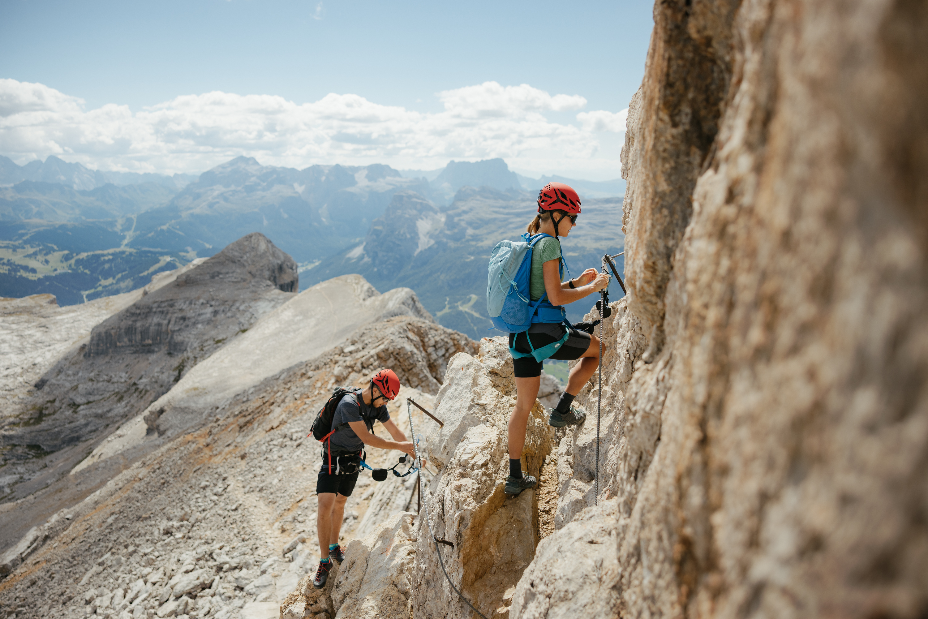 Auf zum Wandern in Alta Badia, rings ums Nature Hotel Delta! Zwei Kletterer mit Helmen sichern sich an einer Felswand in den Bergen