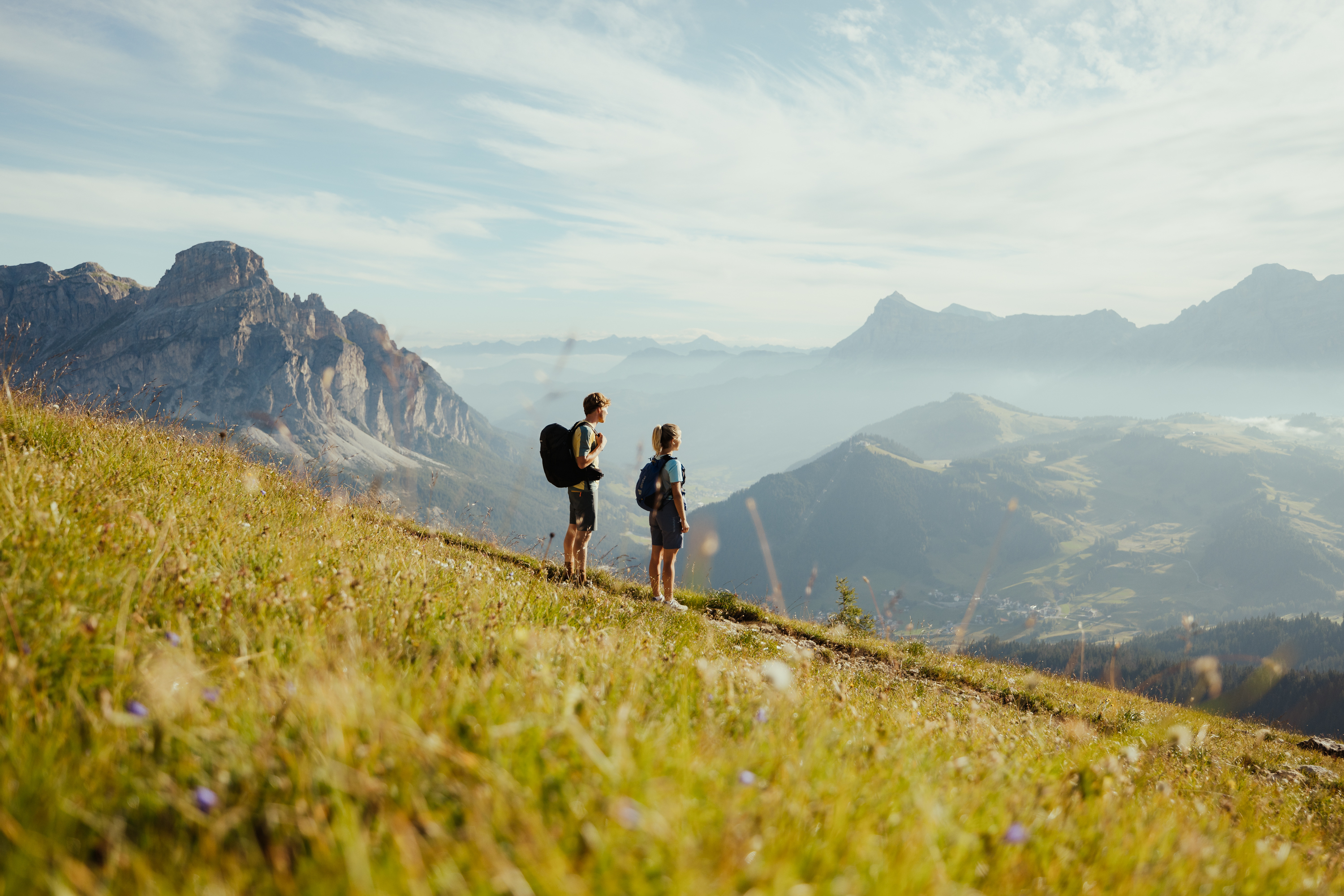 Due escursionisti con zaini su prato di montagna con vista su montagne e valle