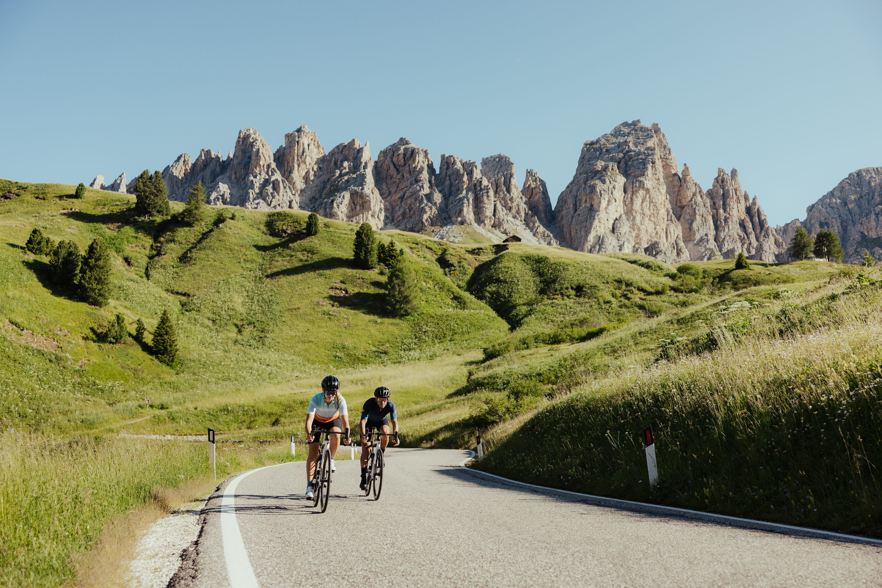 Das ist sehenswert in der Umgebung des Nature Hotel Delta. Zwei Radfahrer auf Bergstraße mit grünen Hügeln und Felsen im Hintergrund