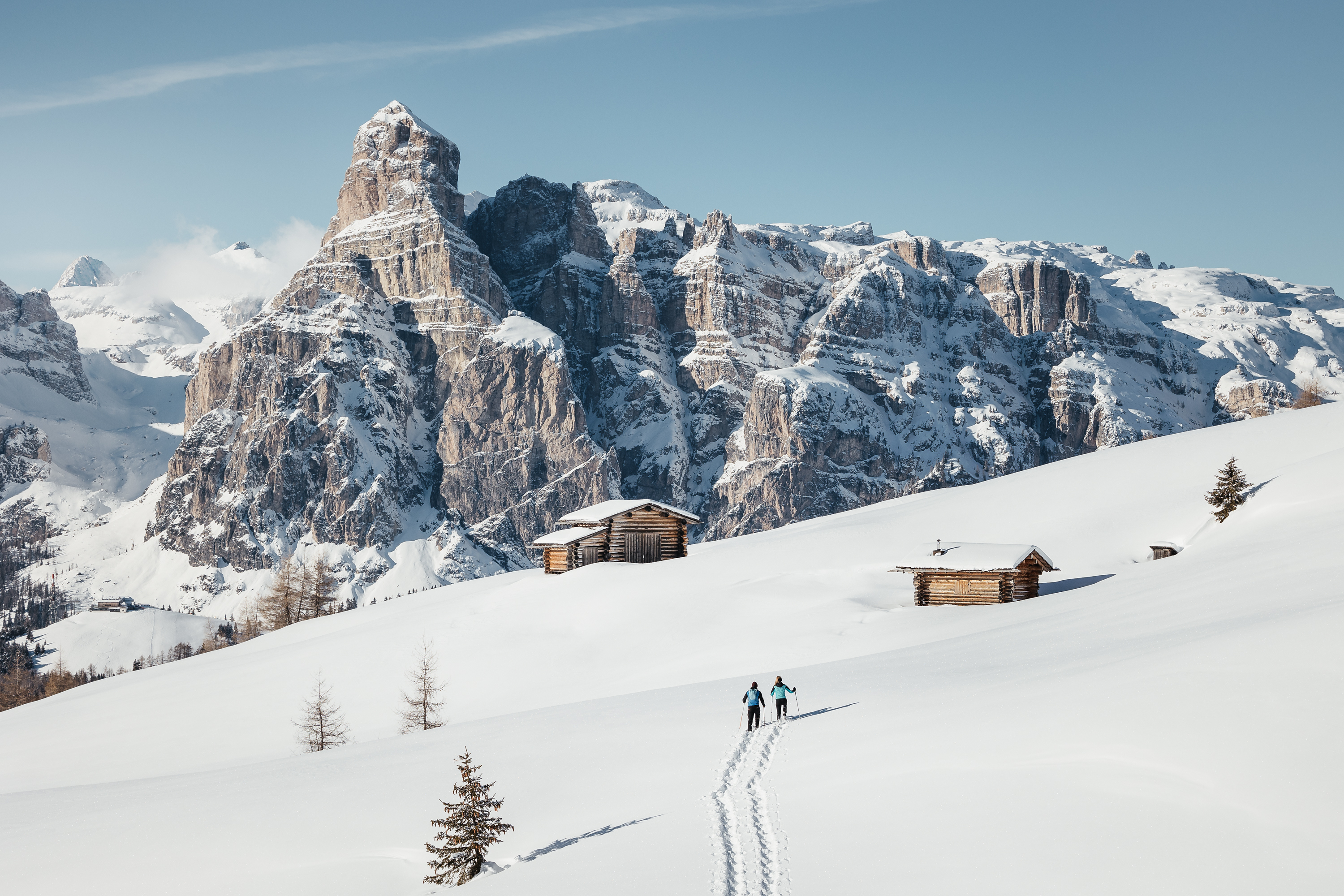 Due sciatori su prato innevato con baite di legno davanti a montagne innevate