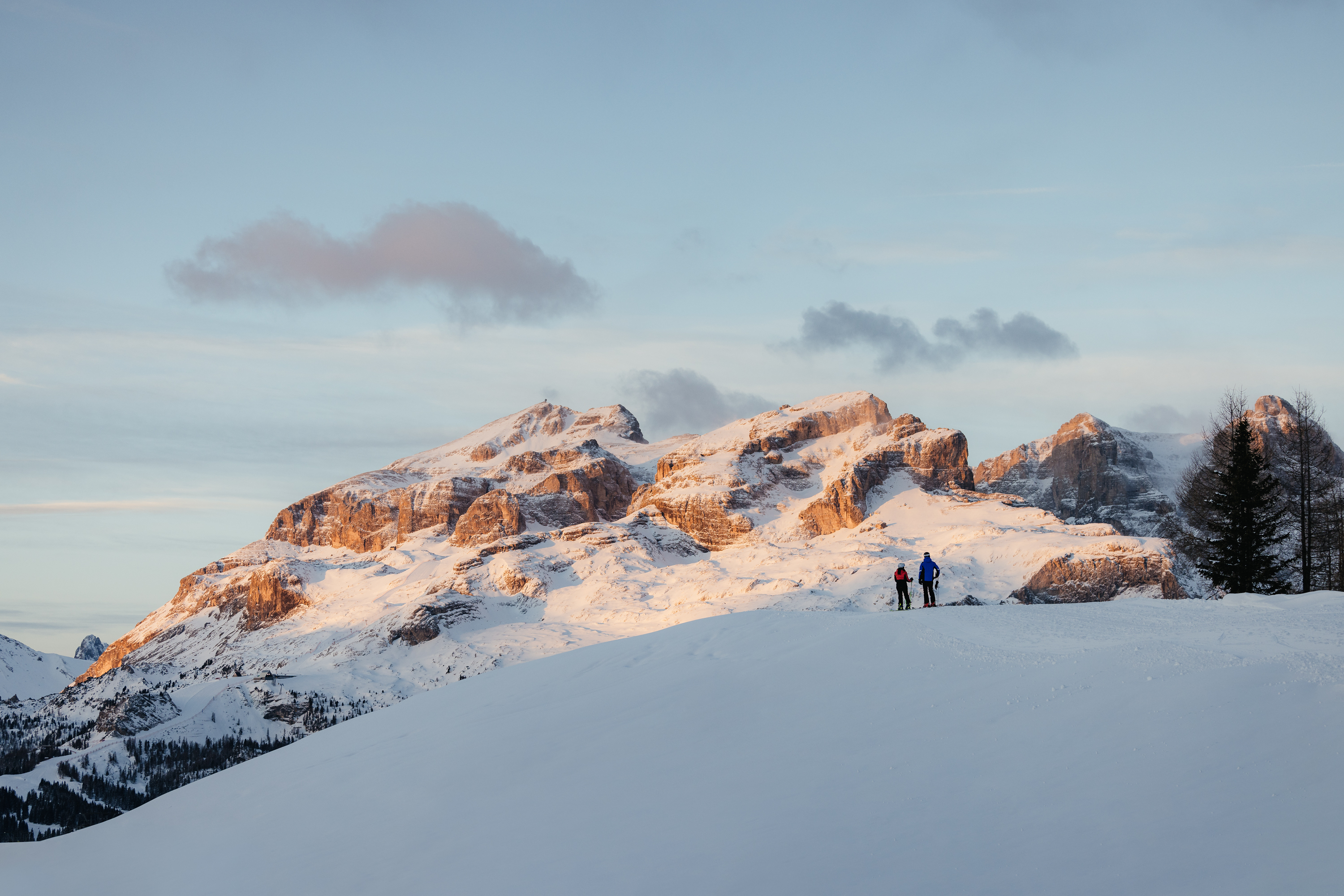Das ist sehenswert in der Umgebung des Nature Hotel Delta. Zwei Skifahrer auf schneebedecktem Hügel mit Sonnenuntergang über Bergen