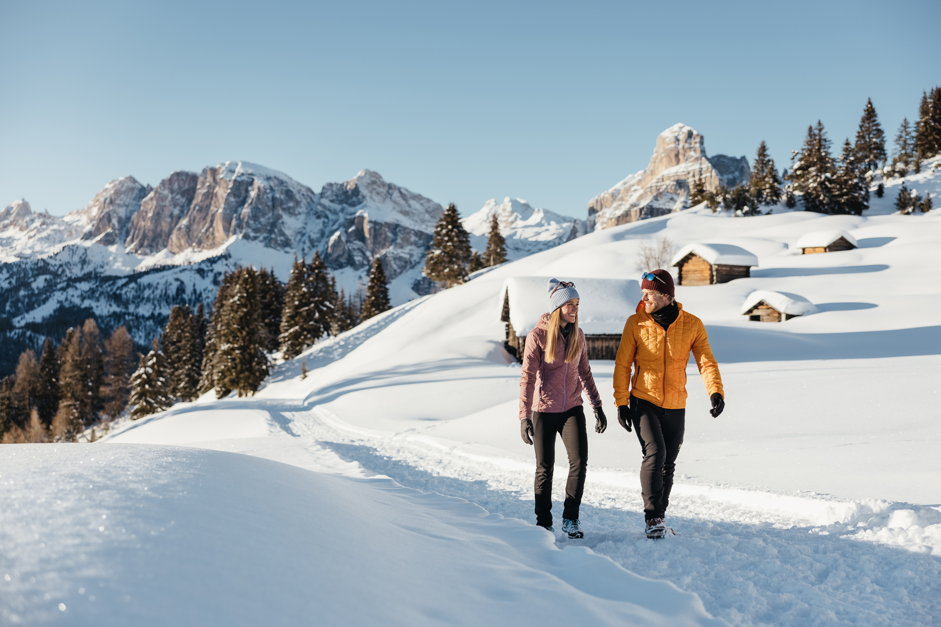 Coppia che cammina su sentiero innevato tra le montagne al sole