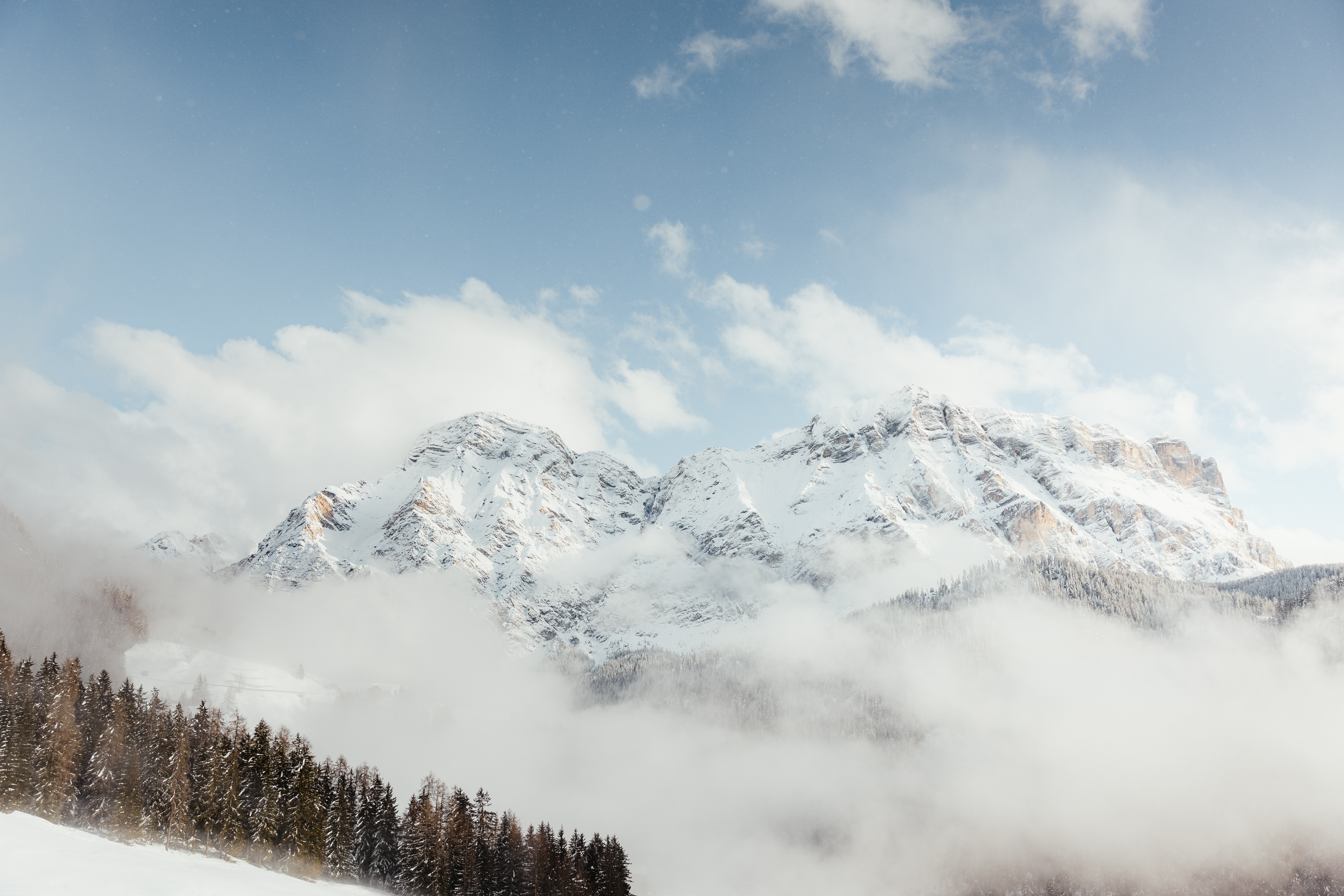 Das ist sehenswert in der Umgebung des Nature Hotel Delta. Schneebedeckte Berge mit Wolken und Nadelwald im Vordergrund