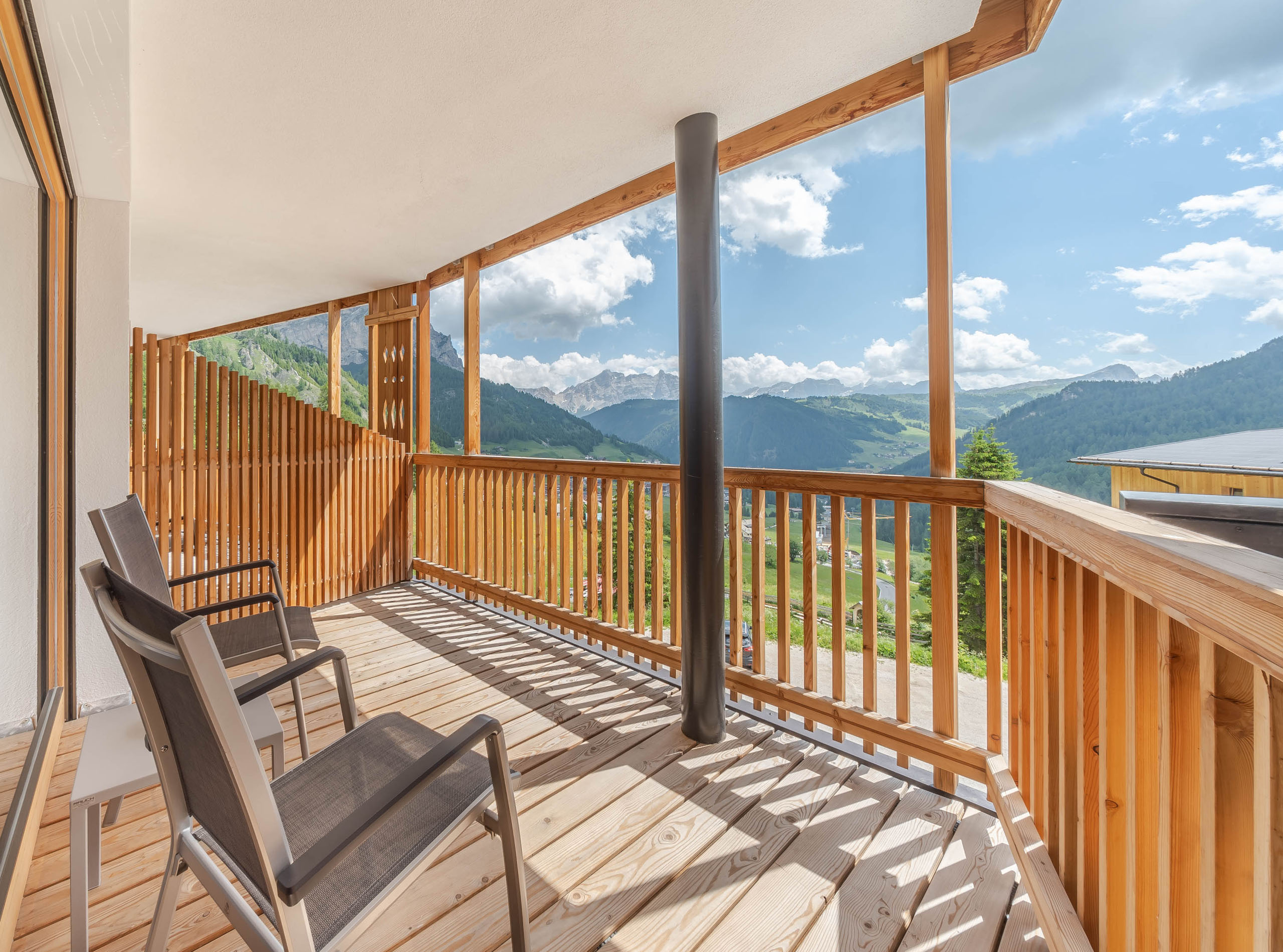 Unser Wellnesshotel in Alta Badia: das Nature Hotel Delta Balkon mit zwei Stühlen und Blick auf Berge bei sonnigem Wetter